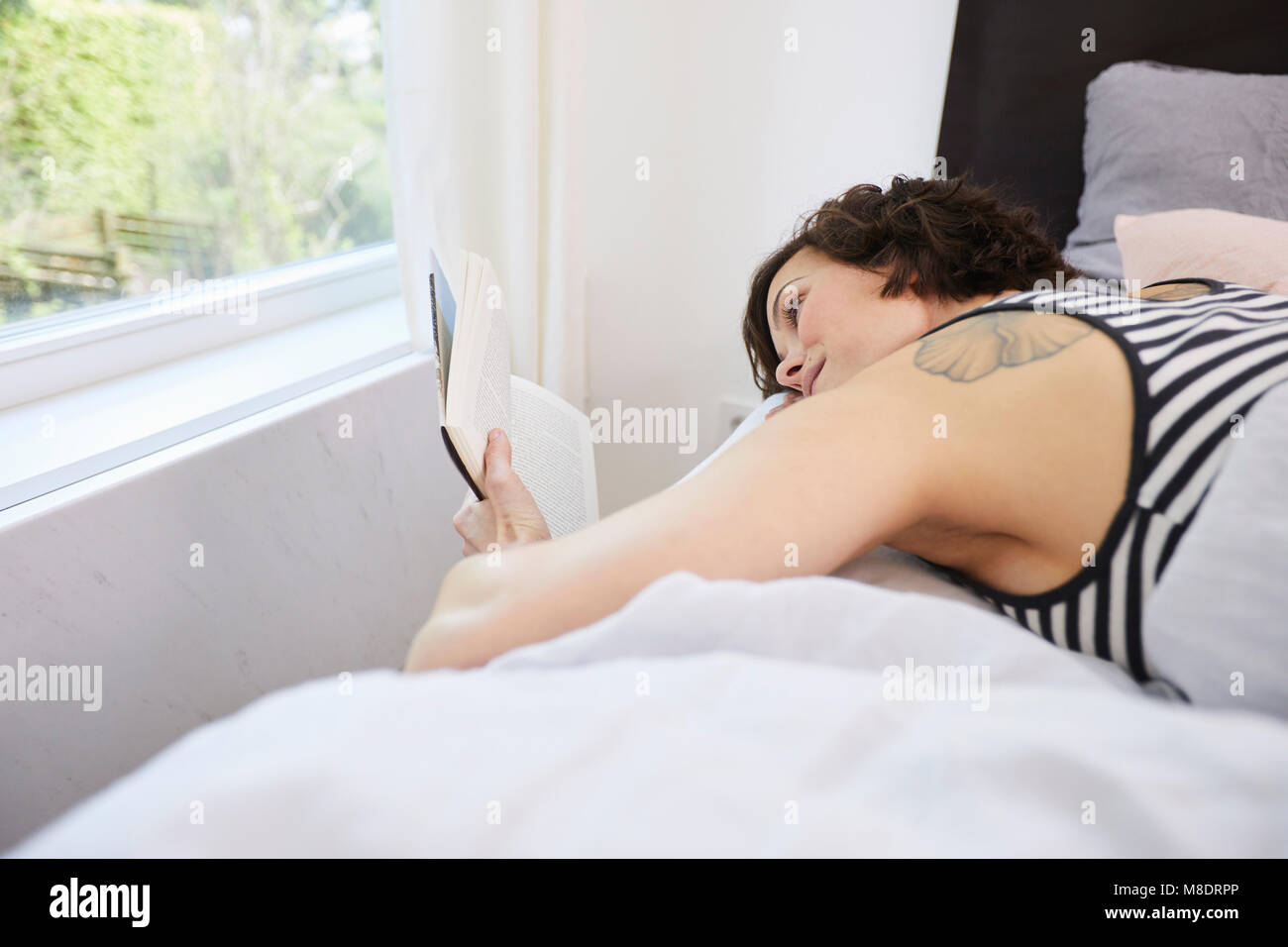 Mid adult woman, détente sur lit, reading book Banque D'Images