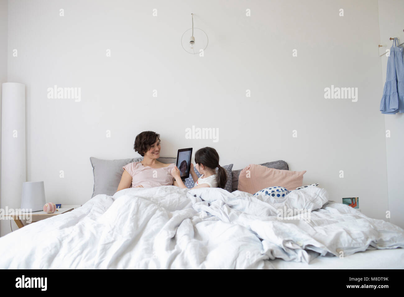 Mère et fille se détendre au lit, fille photographiant mère using digital tablet Banque D'Images