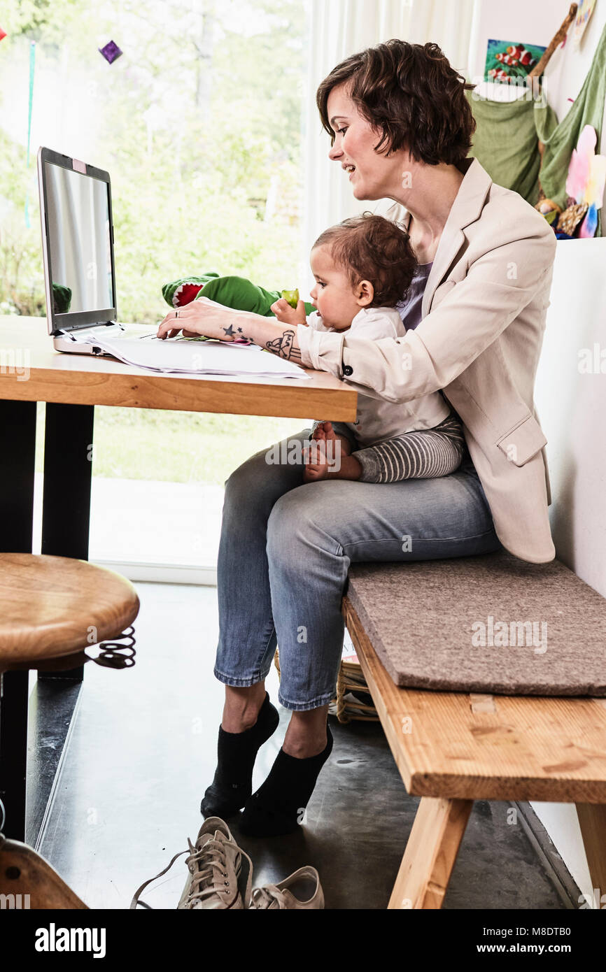Mère tenant assis avec sa petite fille, working on laptop Banque D'Images