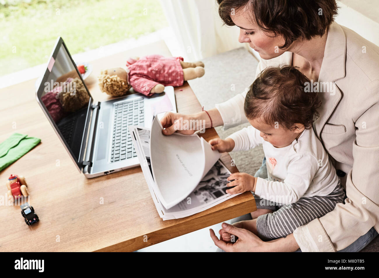 Mère assise avec sa petite fille, à l'entremise de la paperasserie, ordinateur portable sur table devant elle Banque D'Images