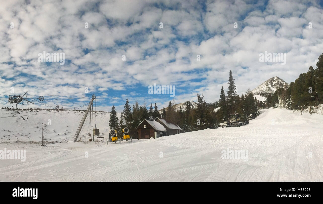 Piste rouge vide sur Strbske Pleso, Solisko ski aux beaux jours de printemps avec des nuages dans l'arrière-plan et en premier plan de neige damée. Banque D'Images