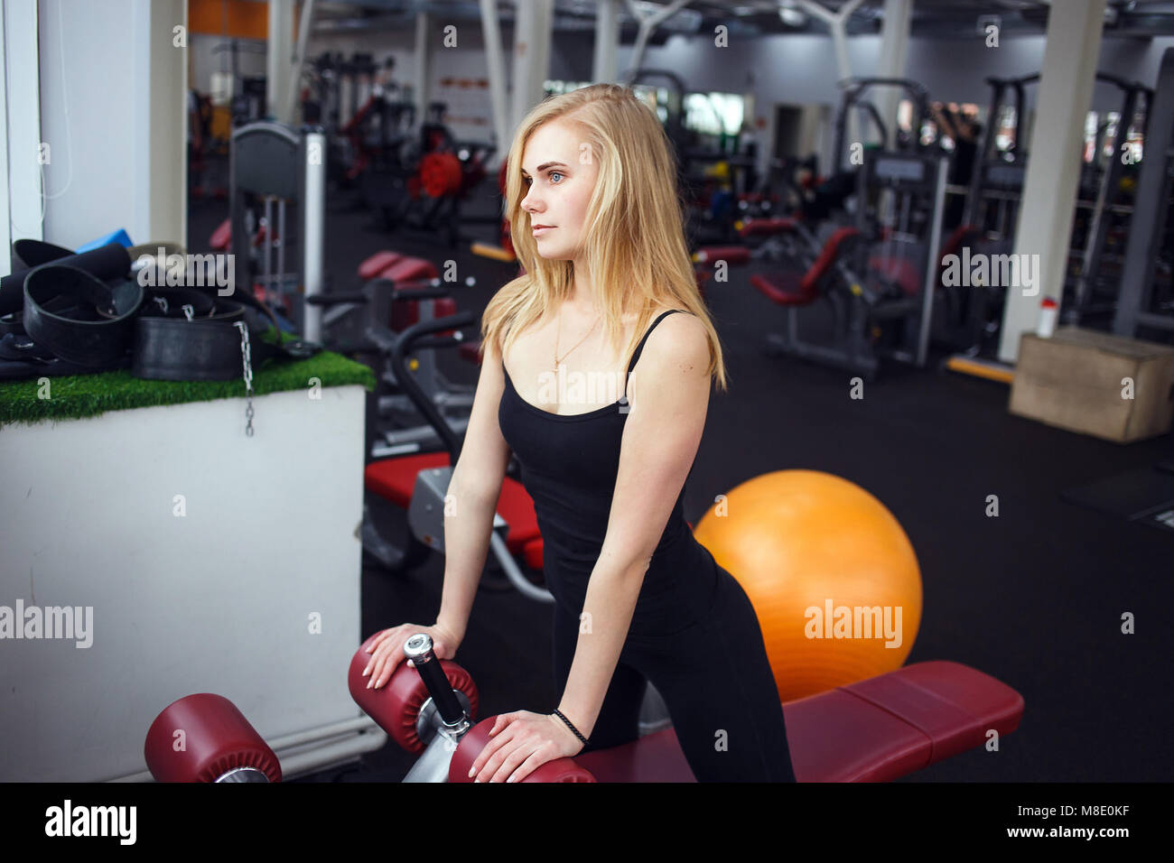 Jeune fille blonde dans la salle de sport. Elle porte un pantalon foncé et T-shirt noir. Elle se détendre et à la fenêtre de Banque D'Images