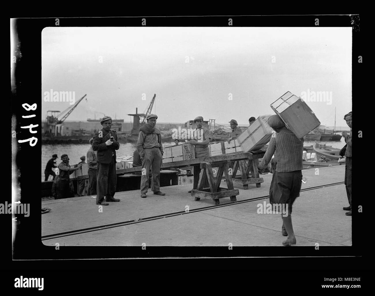 Cette photographie représente le port animé de tel Aviv, où les travailleurs chargent des briquets avec des boîtes orange. Il reflète les activités commerciales et maritimes du port, plaque tournante importante pour le commerce et le transport. Banque D'Images
