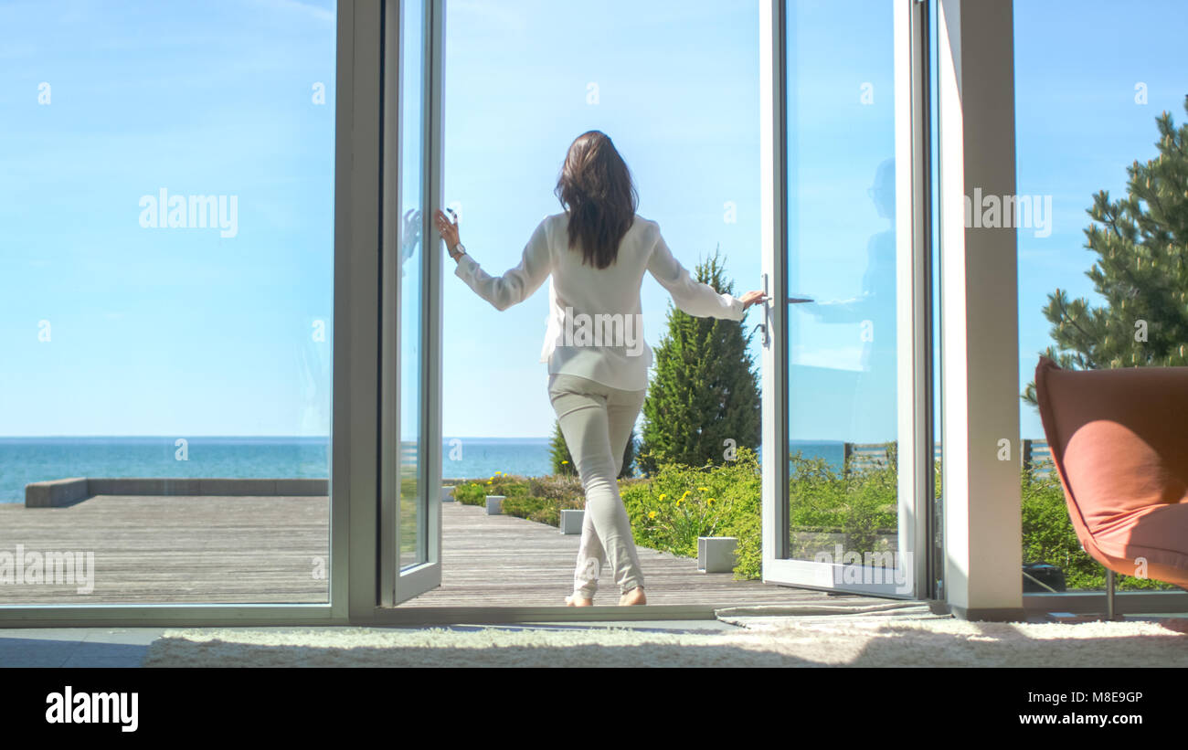 Tiré d'une belle brune avec les cheveux l'ouverture des portes du balcon et la marche à pied sur terrasse ensoleillée avec vue sur la mer. Banque D'Images