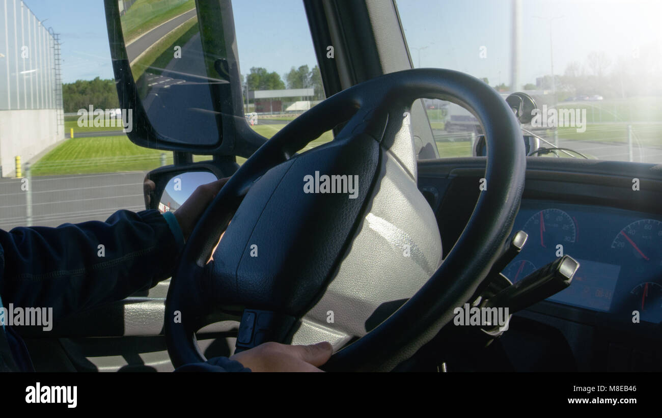 À l'intérieur de la cabine du conducteur du camion au volant de son gros véhicule sur la route. Entrepôts industriels sont considérés hors de la fenêtre. Banque D'Images