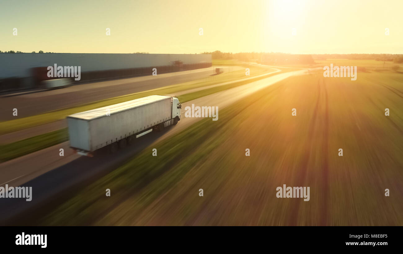 Suivi de l'antenne de tir semi blanc camion avec remorque Cargo transitant par l'entrepôt industriel, région rurale. Le soleil brille et le ciel est bleu. B Banque D'Images