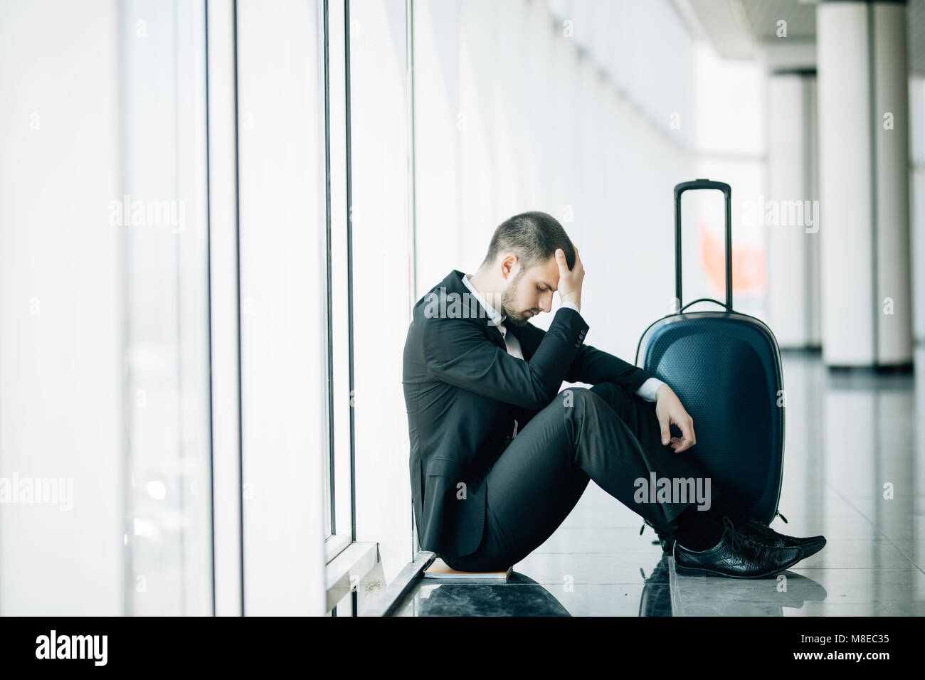Business man sitting at the airport terminal sur le plancher avec valise vol retardé, deux mains se touchent en tête, maux de tête, attendant le voyage. Banque D'Images