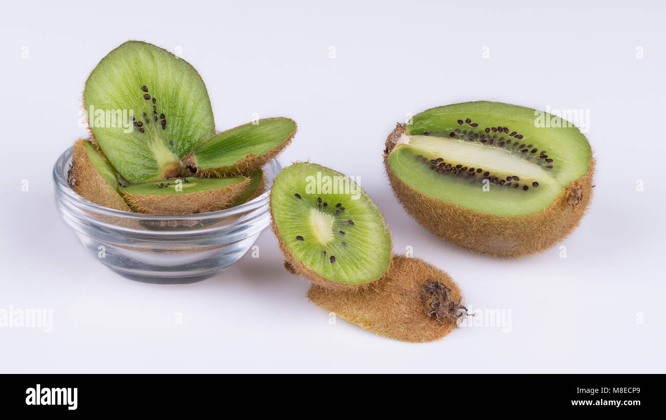 Tranches de morceaux de kiwis avec la peau brune. L'Actinidia deliciosa. Vert décoratif tranches de kiwifruits aigre-doux dans un bol en verre et sur fond blanc. Banque D'Images