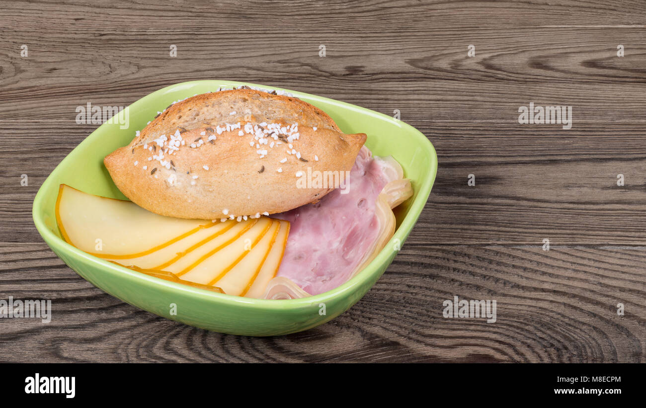 Salé pain, tranches de jarret et fromage sur fond de bois. Le grain entier croquant avec des tranches de pain de viande de porc fumé et edam dans bol vert. Banque D'Images