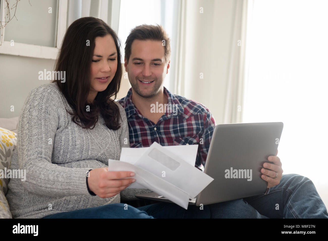 Couple assis sur un canapé et à la lettre, à man holding laptop Banque D'Images