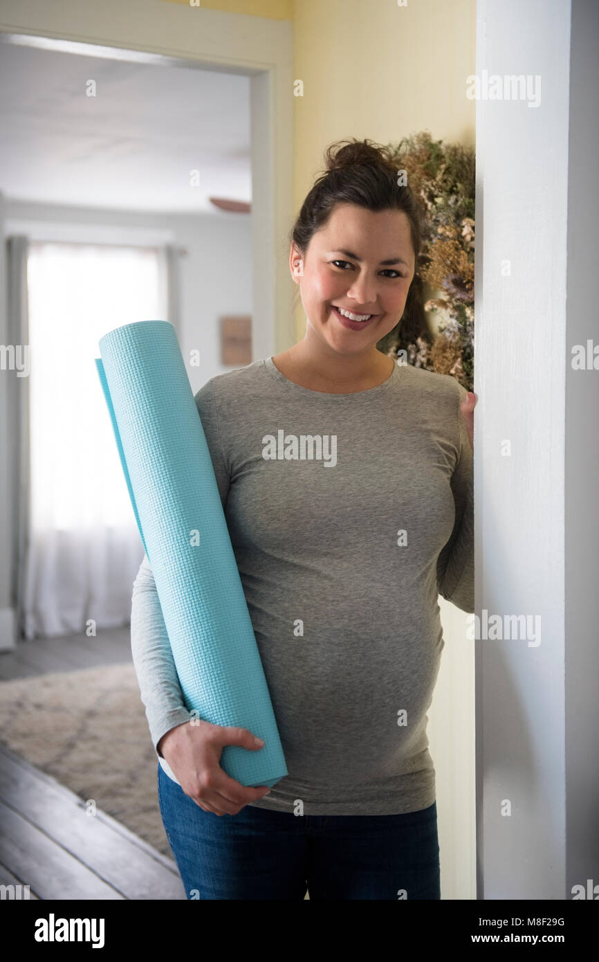 Pregnant woman standing in doorway et tenant l'exercice de mat Banque D'Images Pregnant woman standing in doorway et tenant l'exercice de mat Banque D'Images