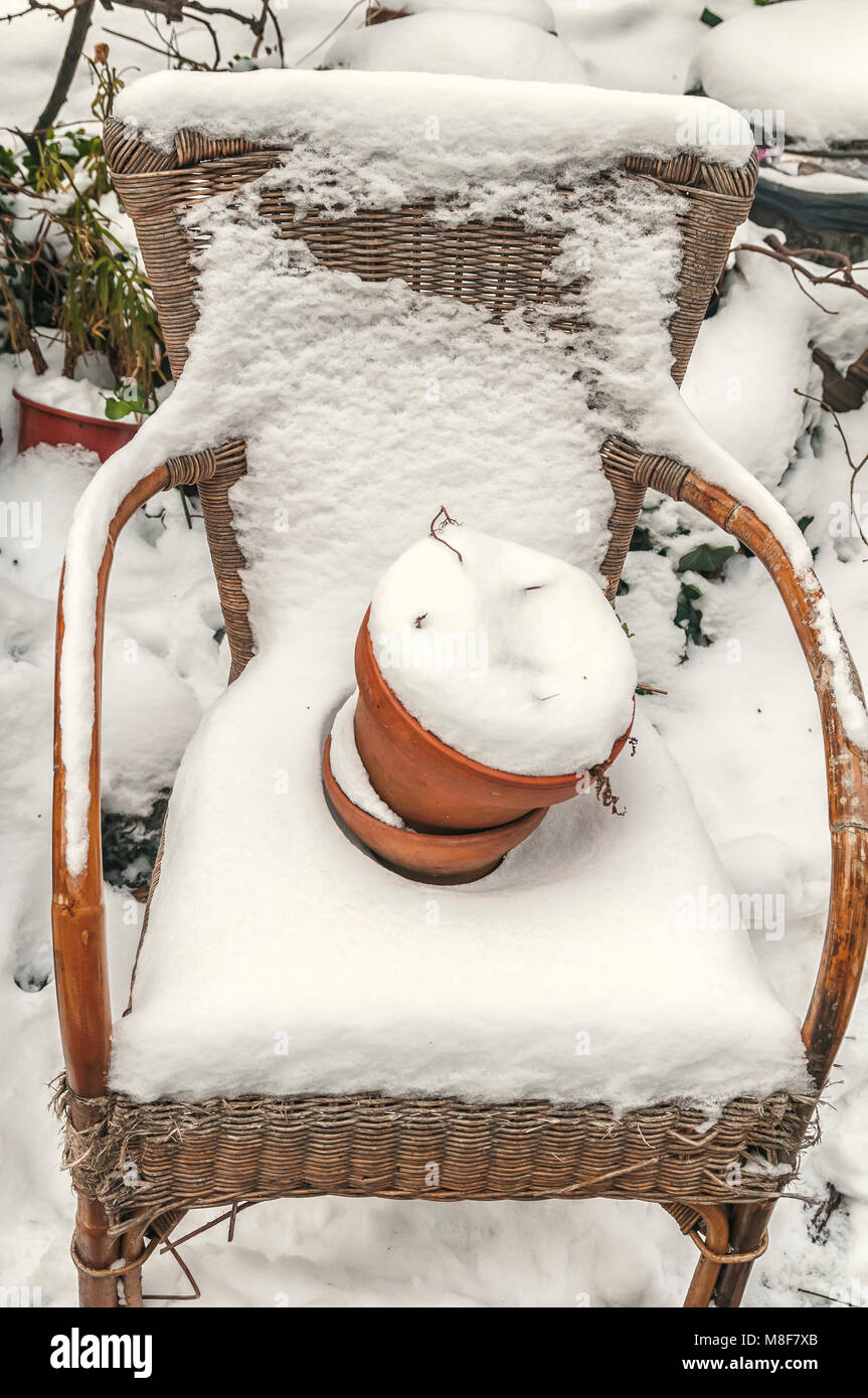 Wicker Chair couverte de neige et un pot de fleur rempli de neige sur le siège Banque D'Images