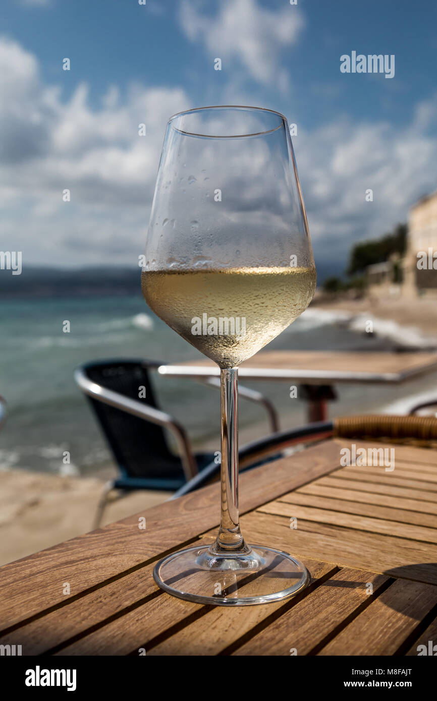 Un verre de vin blanc sur une table avec un arrière-plan flou de la mer et de la ville d'Orebic sur Peljesac en Croate Dalmatie du sud Banque D'Images