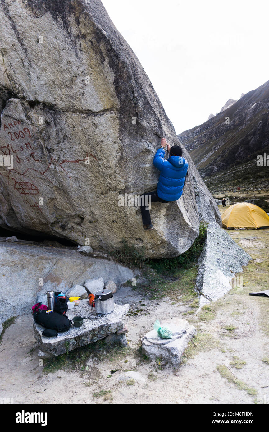 Homme d'alpiniste dans un blue Down Jacket de tenter un grand rocher à un camp de base dans la Cordillère Blanche au Pérou Banque D'Images