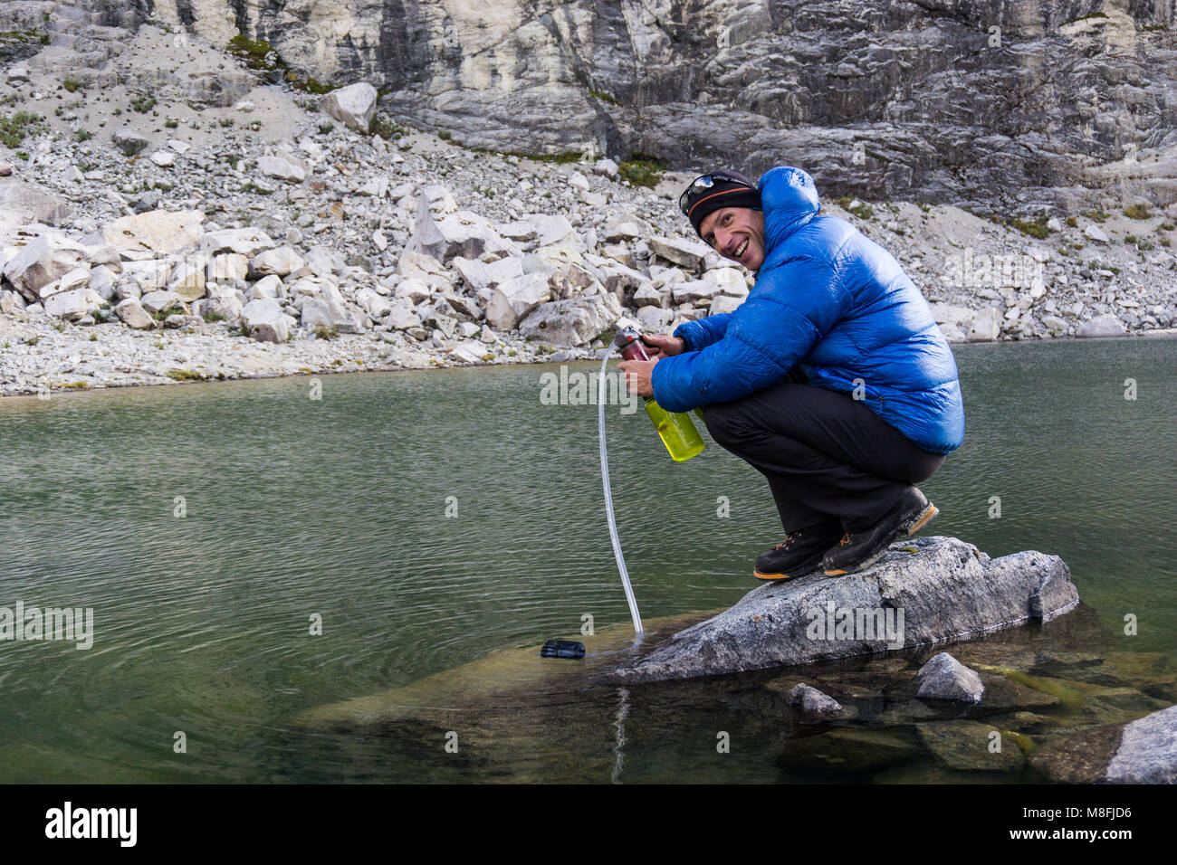 Homme d'alpiniste dans blue Down Jacket filtrer l'eau potable d'un lac dans les Andes au Pérou Banque D'Images Homme d'alpiniste dans blue Down Jacket filtrer l'eau potable d'un lac dans les Andes au Pérou Banque D'Images
