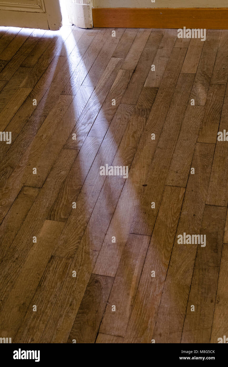 De mystérieux rayons de lumière passant à travers la fente d'une porte ouverte en partie sur un plancher en bois. Banque D'Images