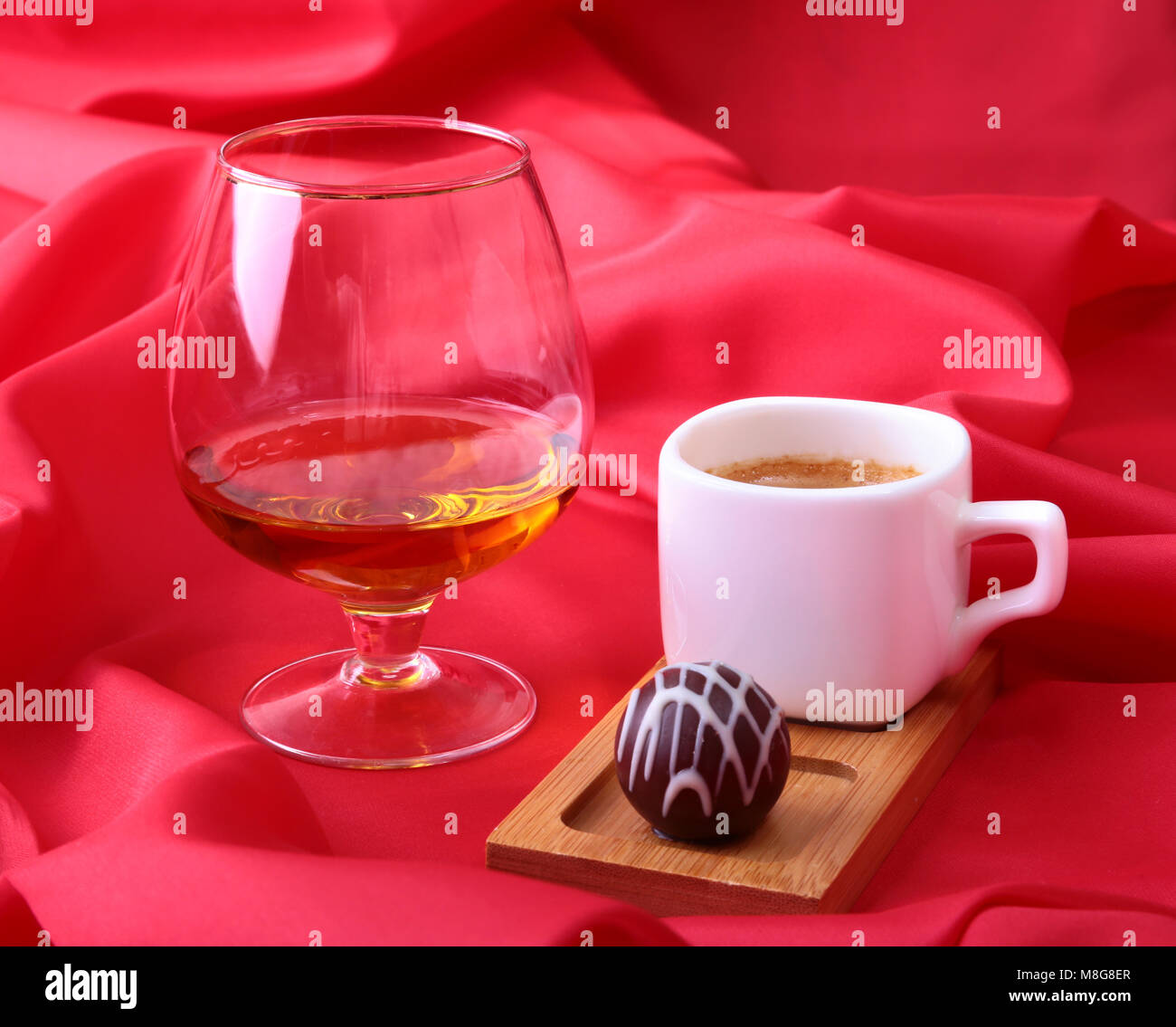 Tasse de café blanc et le cognac dans un verre, des pralines sur fond rouge. Banque D'Images