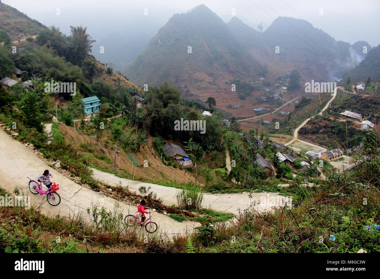 Ha Giang, Vietnam - Mars 18, 2018 : Enfants conduire les vélos dans un village entouré de montagnes et de brouillard dans l'extrême nord de la province du Vietnam Banque D'Images