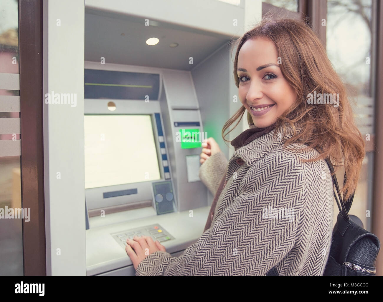 Jeune femme heureuse avec carte de crédit en utilisant un guichet automatique Banque D'Images