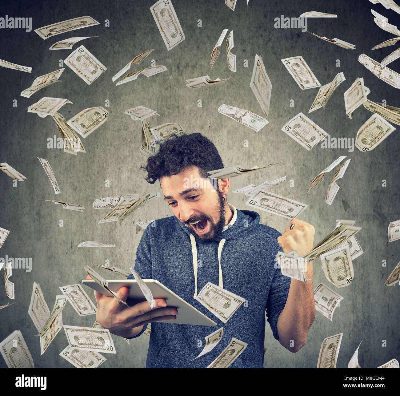 Homme heureux à l'aide d'un ordinateur tablette et posant avec triomphe sous battant billets d'un dollar. Banque D'Images