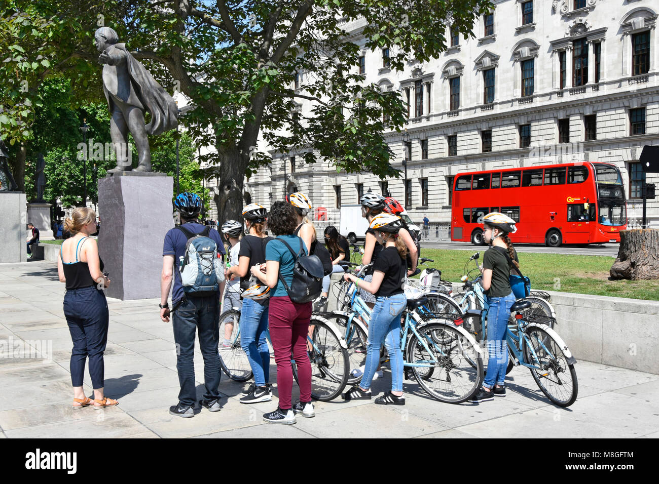 Groupe de cyclotouristes & guide touristique avec location de vélos personnes autour de statue de David Lloyd George au Parlement Square London England UK bus rouge Banque D'Images