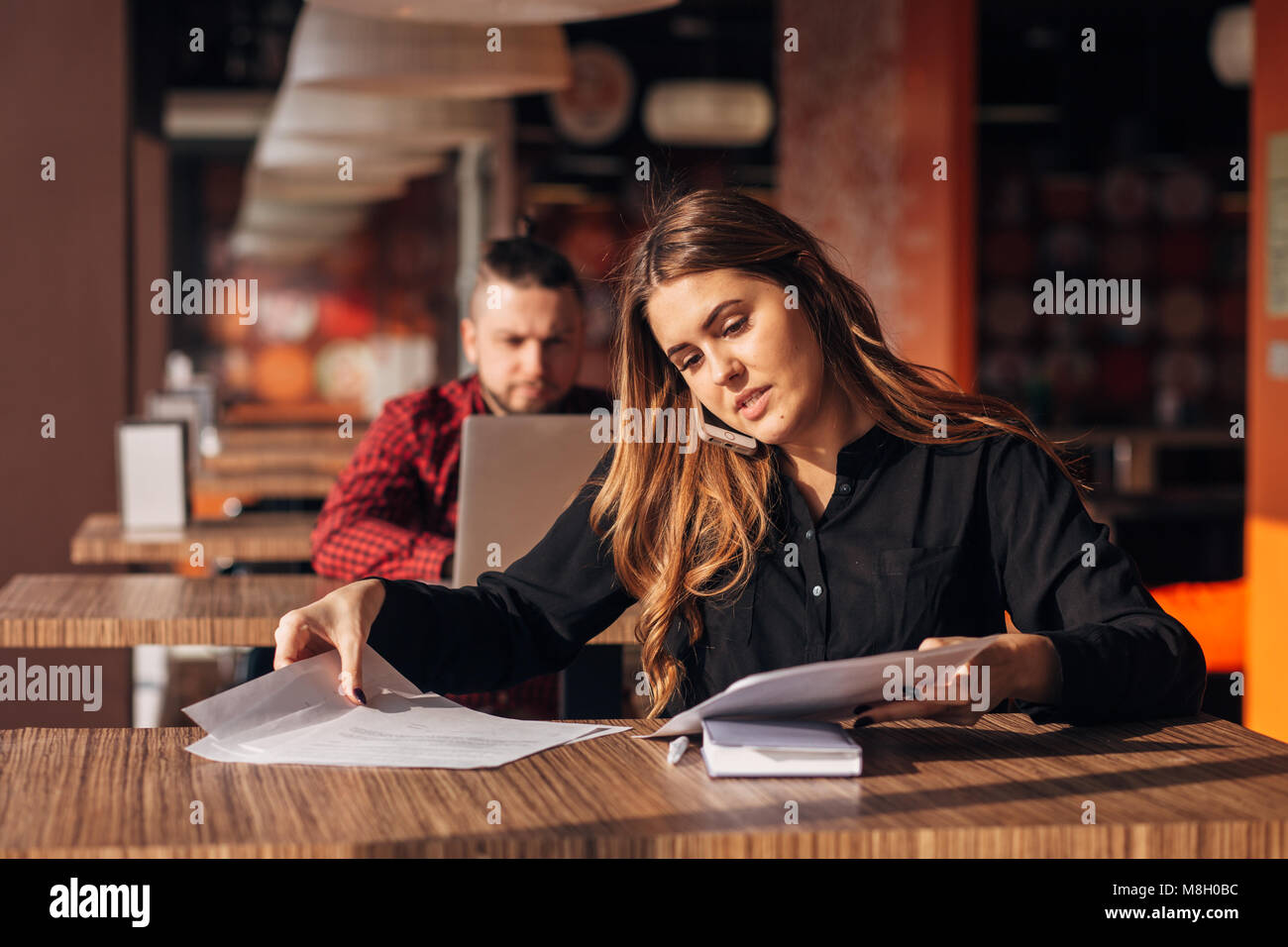 Happy businesswoman sitting at the table et parler au téléphone en cafe.bearded freelancer dans l'arrière-plan Banque D'Images
