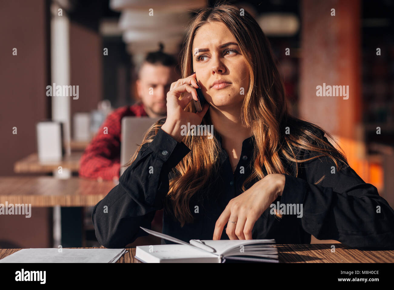 Businesswoman assis à la table et à parler au téléphone en cafe.bearded freelancer dans l'arrière-plan Banque D'Images
