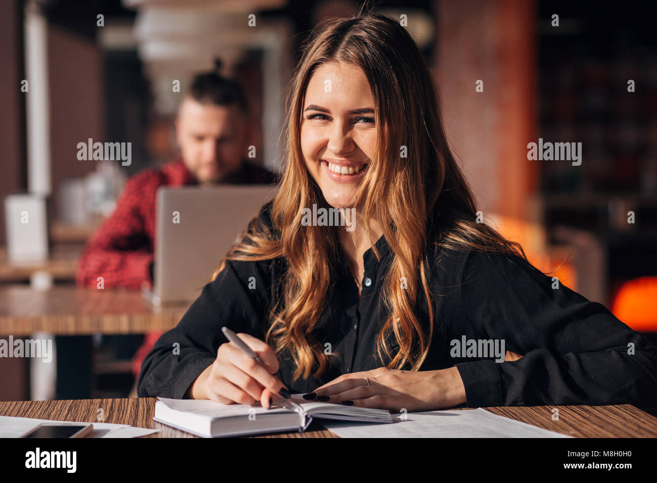 Portrait d'une femme confiante en prenant des notes dans un bloc-notes tout en étant assis à table dans un café à l'intérieur et looking at camera Banque D'Images