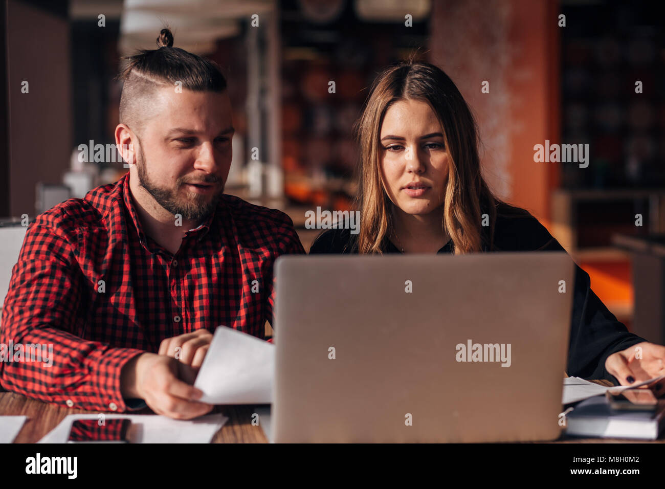 Les jeunes pigistes man and woman sitting in a cafe et de travail pour un ordinateur portable. Banque D'Images