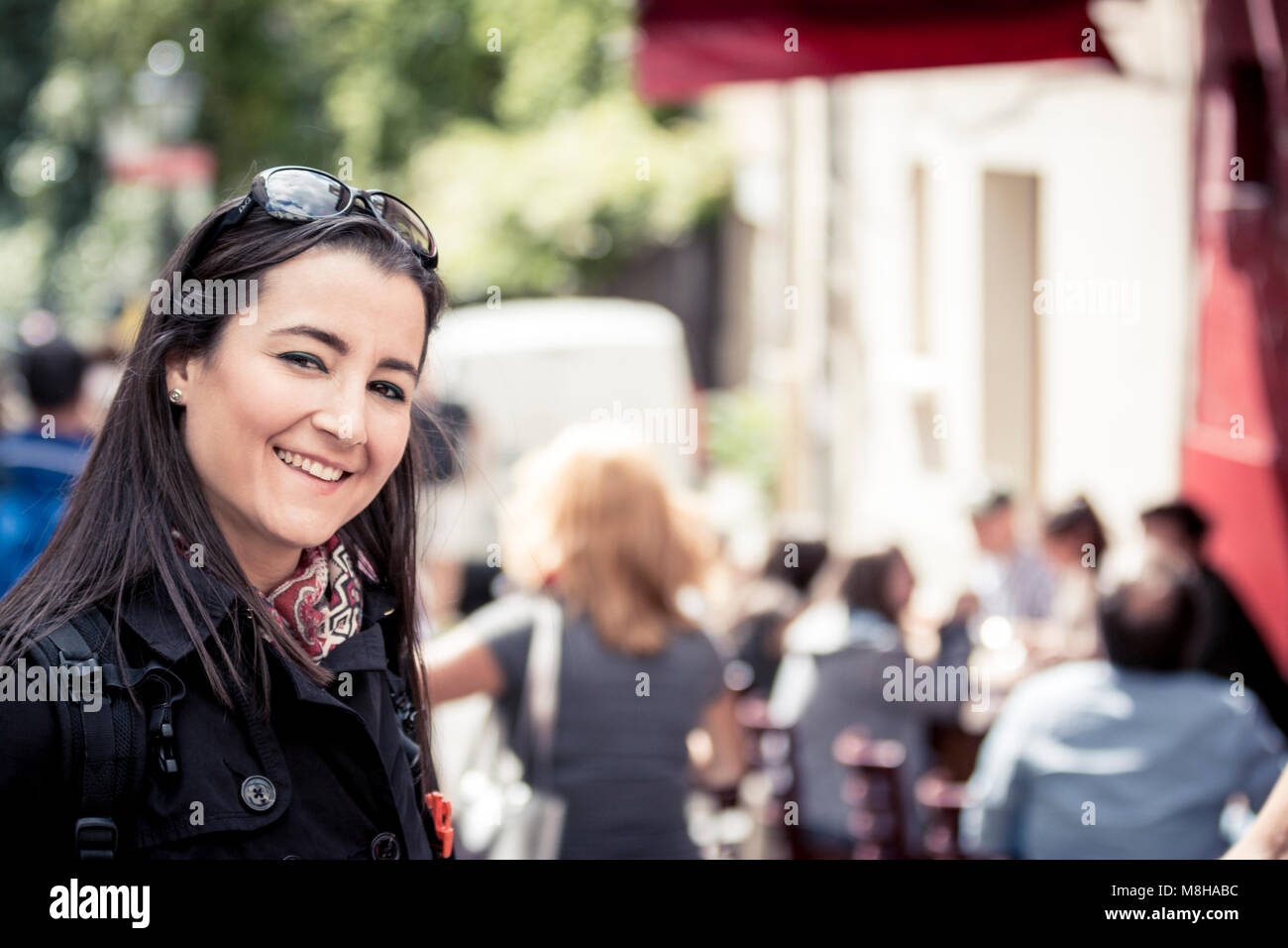Jeune femme en sunglasses smiling at camera sur fond de rue ensoleillée occupé Banque D'Images