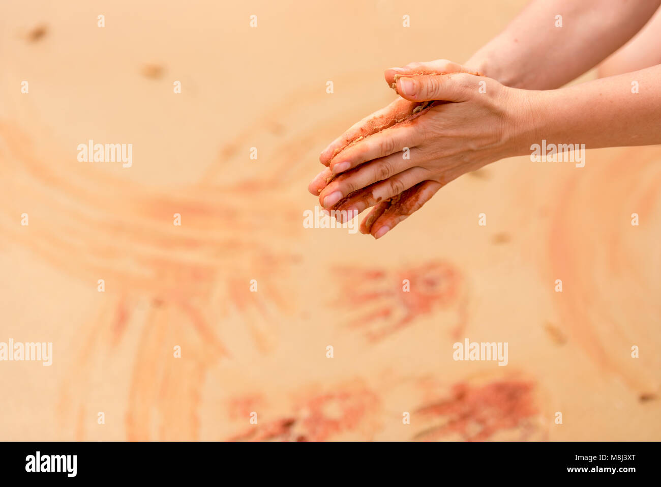 Femme mains créer des formes avec du sable rouge sur la plage dans un style d'art autochtone, modèle pour des projets créatifs Banque D'Images