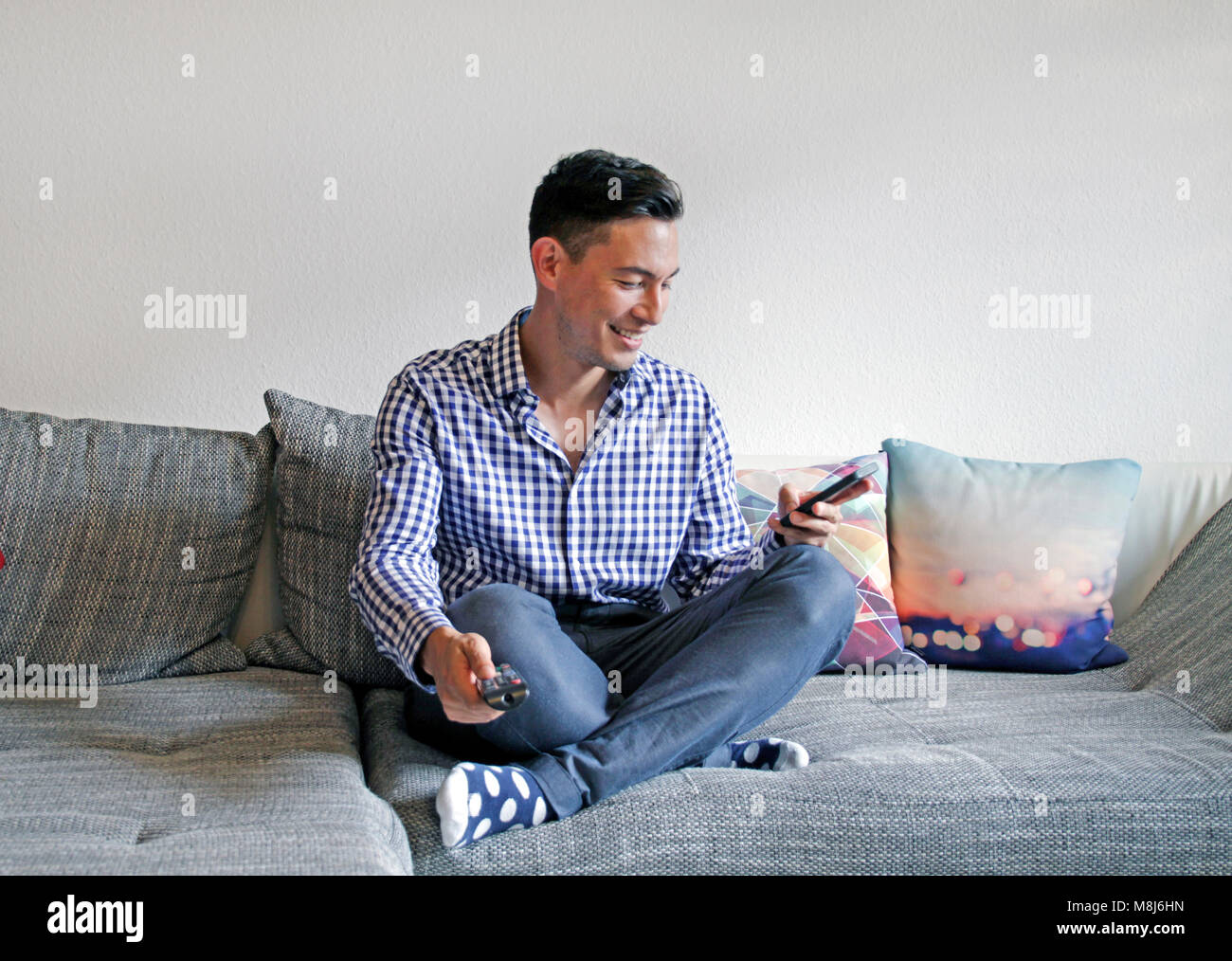 Smiling man avec télécommande et smartphone - deuxième écran Banque D'Images