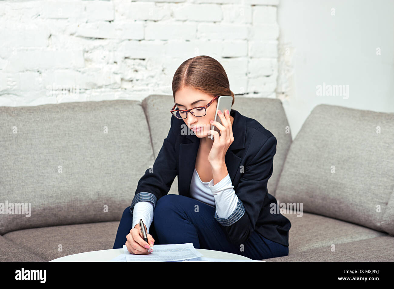 Belle jeune business woman sitting on sofa at office avec des documents et du café Banque D'Images