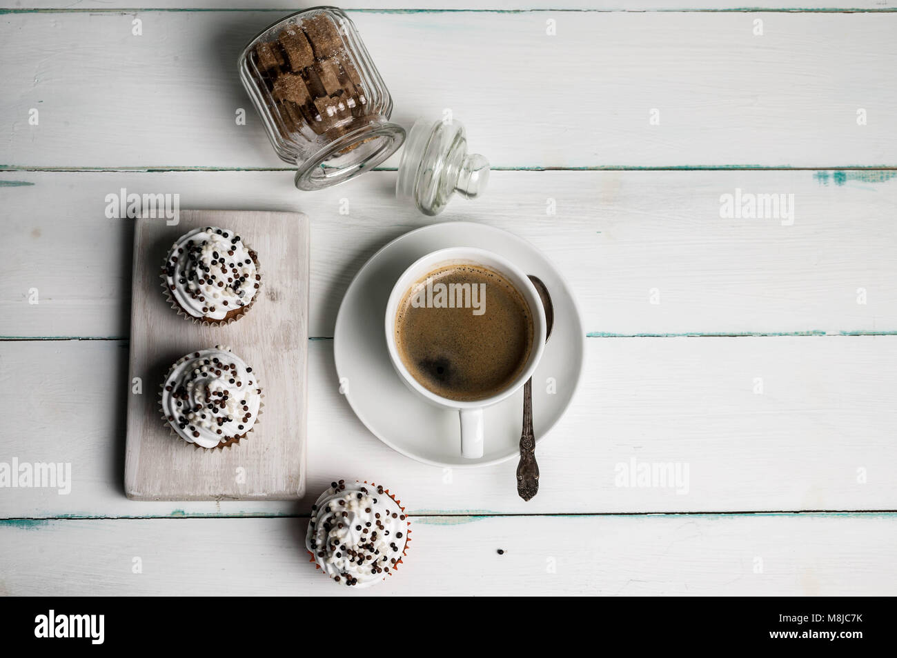 Cupcakes à la vanille crème au beurre avec du chocolat topping et tasse de café sur une planche en bois sur un fond clair. Vue d'en haut Banque D'Images