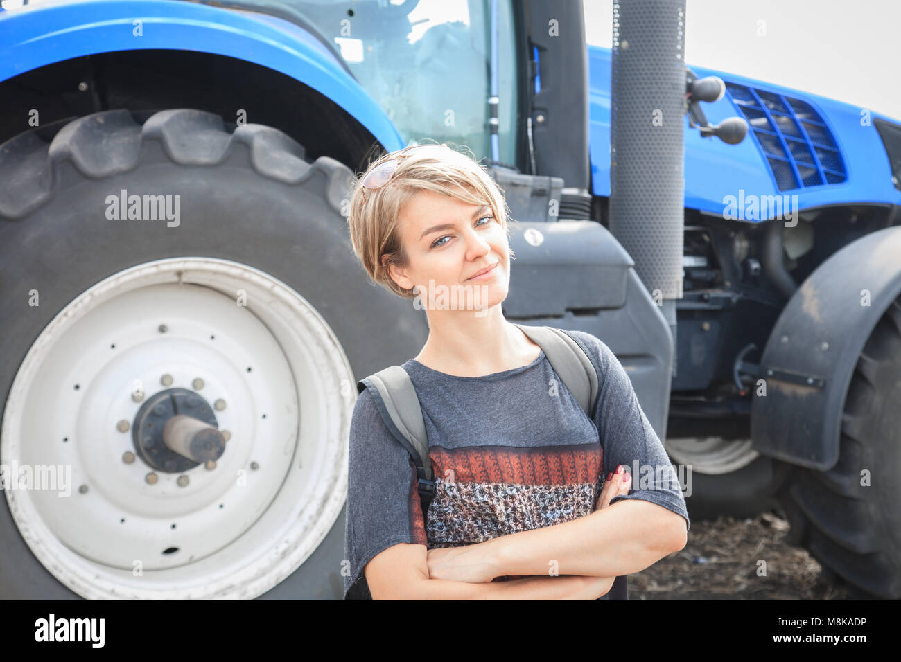 Jolie Jeune femme debout sur le terrain avec le tracteur en arrière-plan Banque D'Images