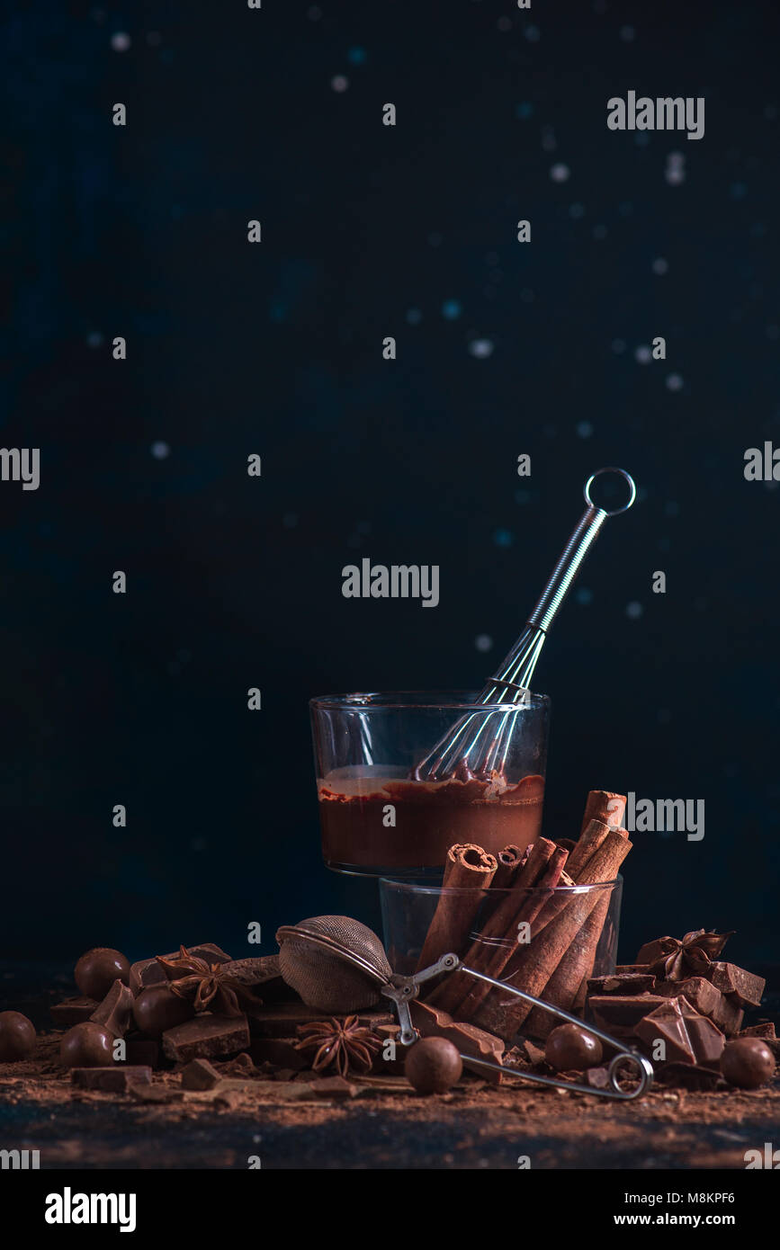 Ingrédients chocolat fait maison sur un fond sombre. Vitrage avec un fouet, la cannelle, casse de pièces en chocolat, poudre de cacao et à l'anis étoile. Dessert co Banque D'Images