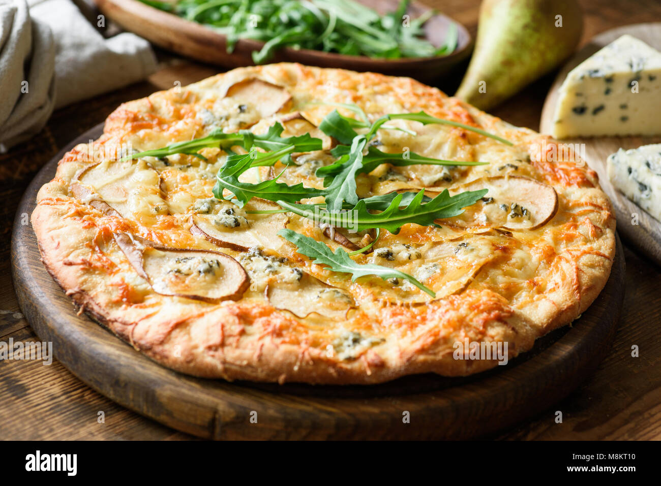 Poire et fromage à pizza garnie de roquette fraîche sur planche à pizza, vue rapprochée Banque D'Images