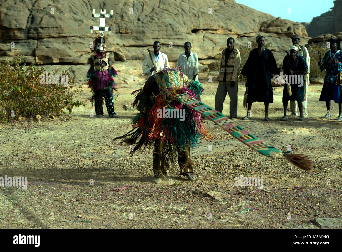 Un groupe de danseurs masqués Dogon regarder un homme portant une coiffe imposante effectuer sa part dans une danse traditionnelle. Pays dogon, Mali, Afrique de l'Ouest. Banque D'Images