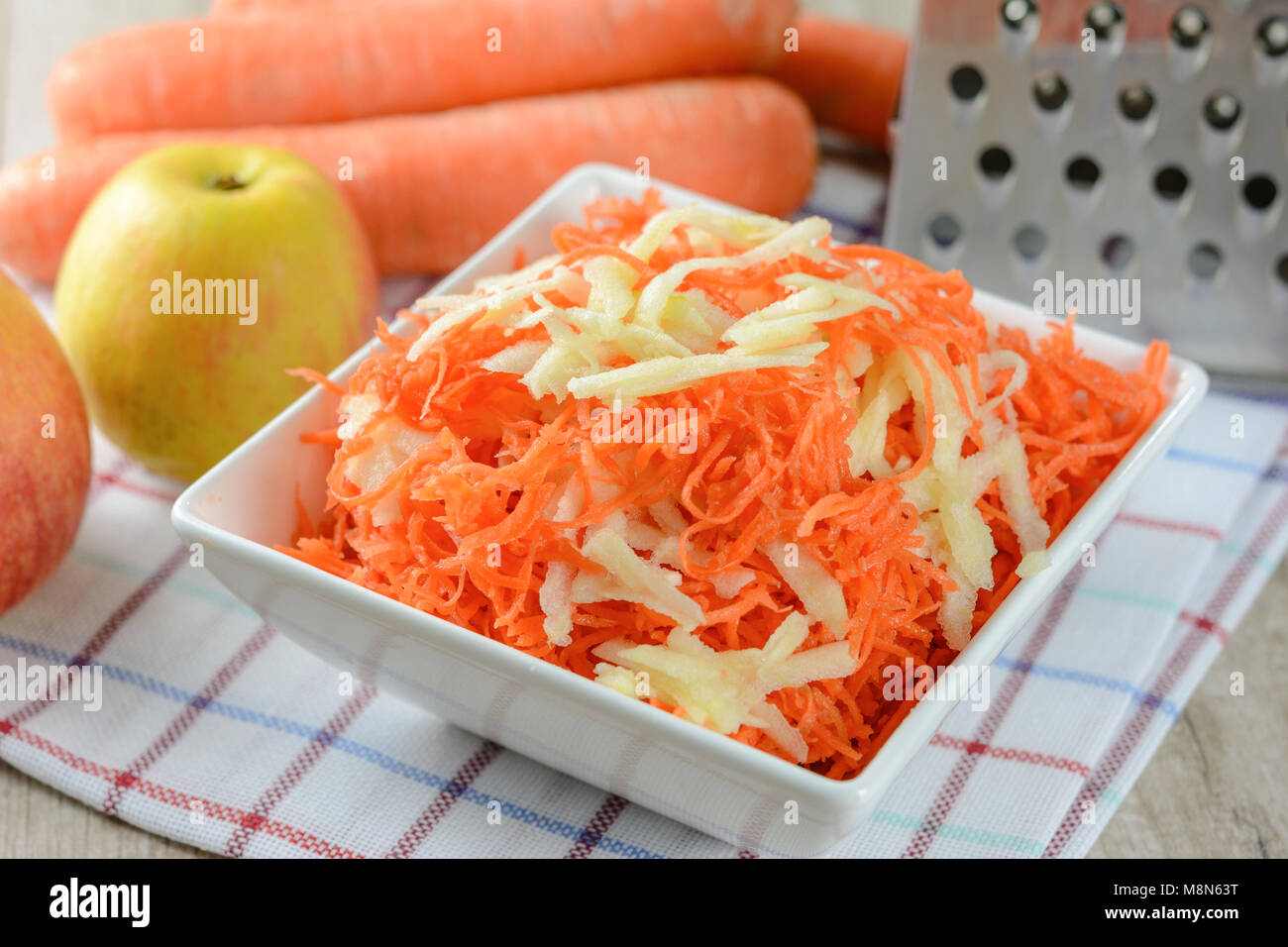 Concept de préparer une salade saine - carottes râpées avec Apple dans un plateau blanc sur fond de râpes, les carottes et les pommes Banque D'Images