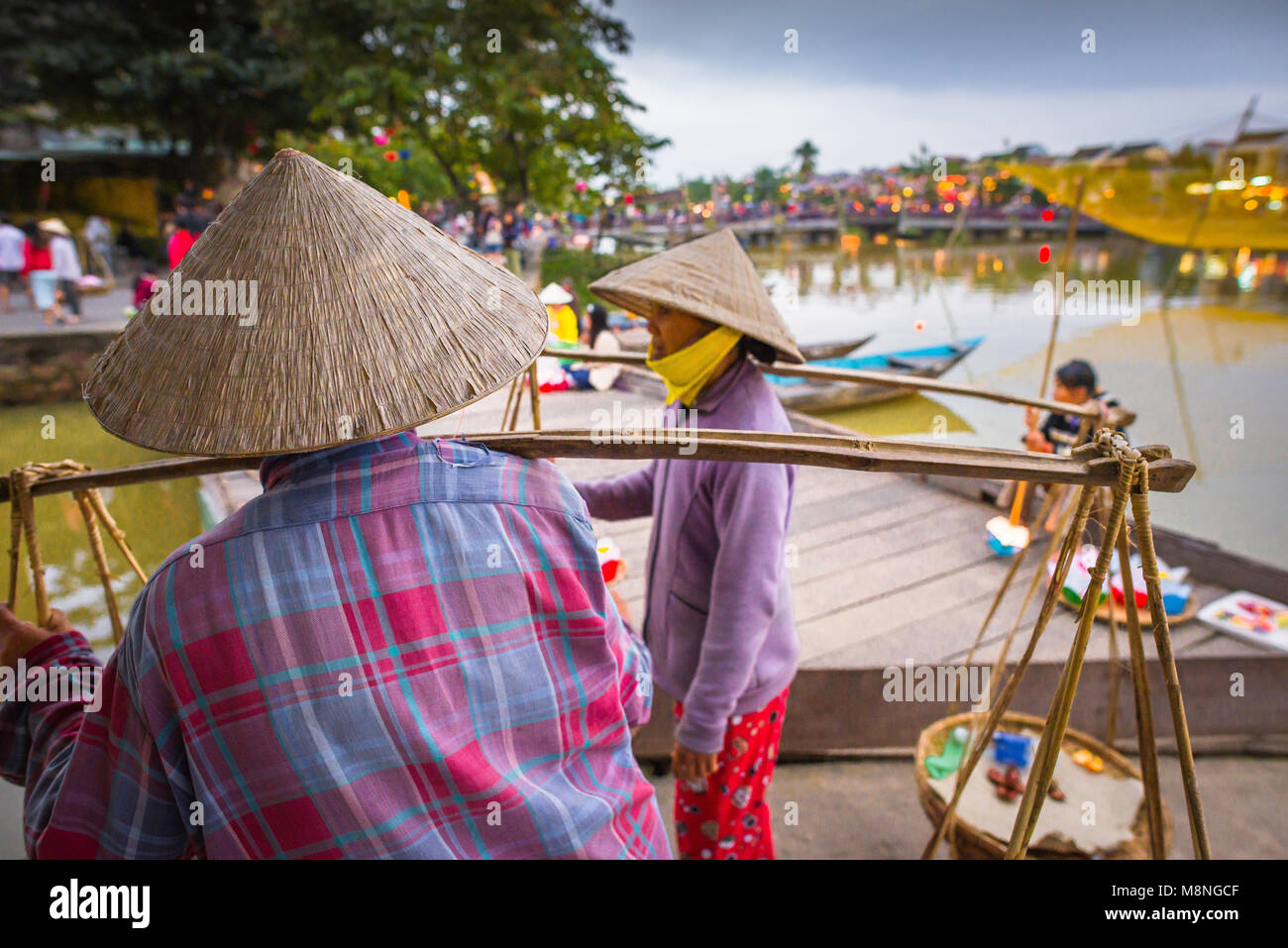 Femmes vietnamiennes, vue de deux vendeuses portant des chapeaux coniques vietnamiens discutant le long du front de mer à Hoi an, côte centrale, Vietnam. Banque D'Images