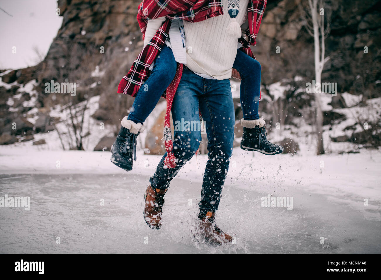 Jeune homme porte sa petite amie sur le dos à travers flaque d'eau fondue avec le vol à part les projections d'eau. Banque D'Images