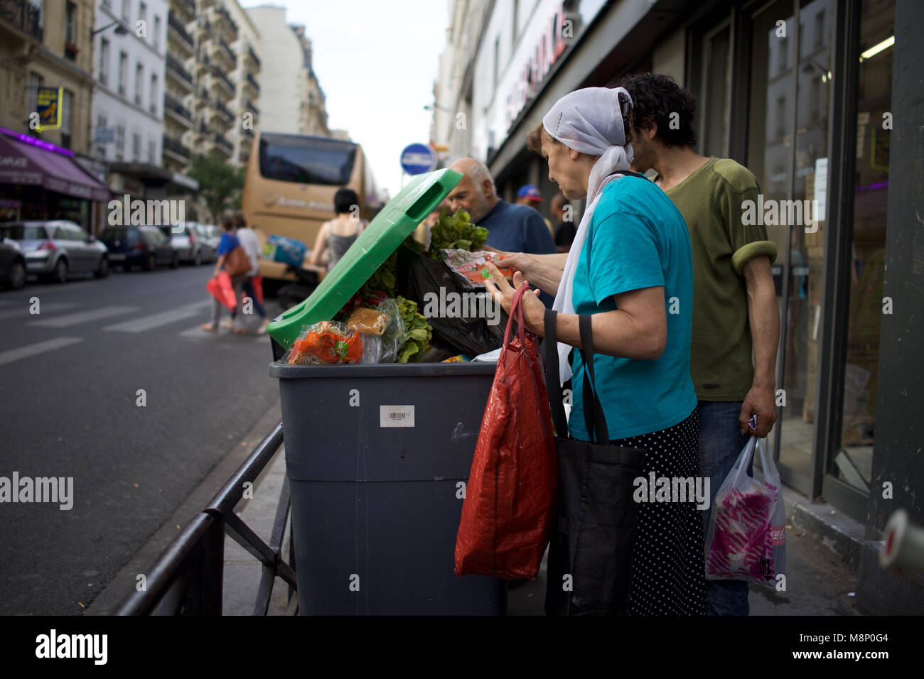 Femme noire handicapée avec béquille et d'autres personnes regardent à travers les déchets alimentaires dans la poubelle, supermarché extérieur, rue de Clignancourt, Paris, France Banque D'Images