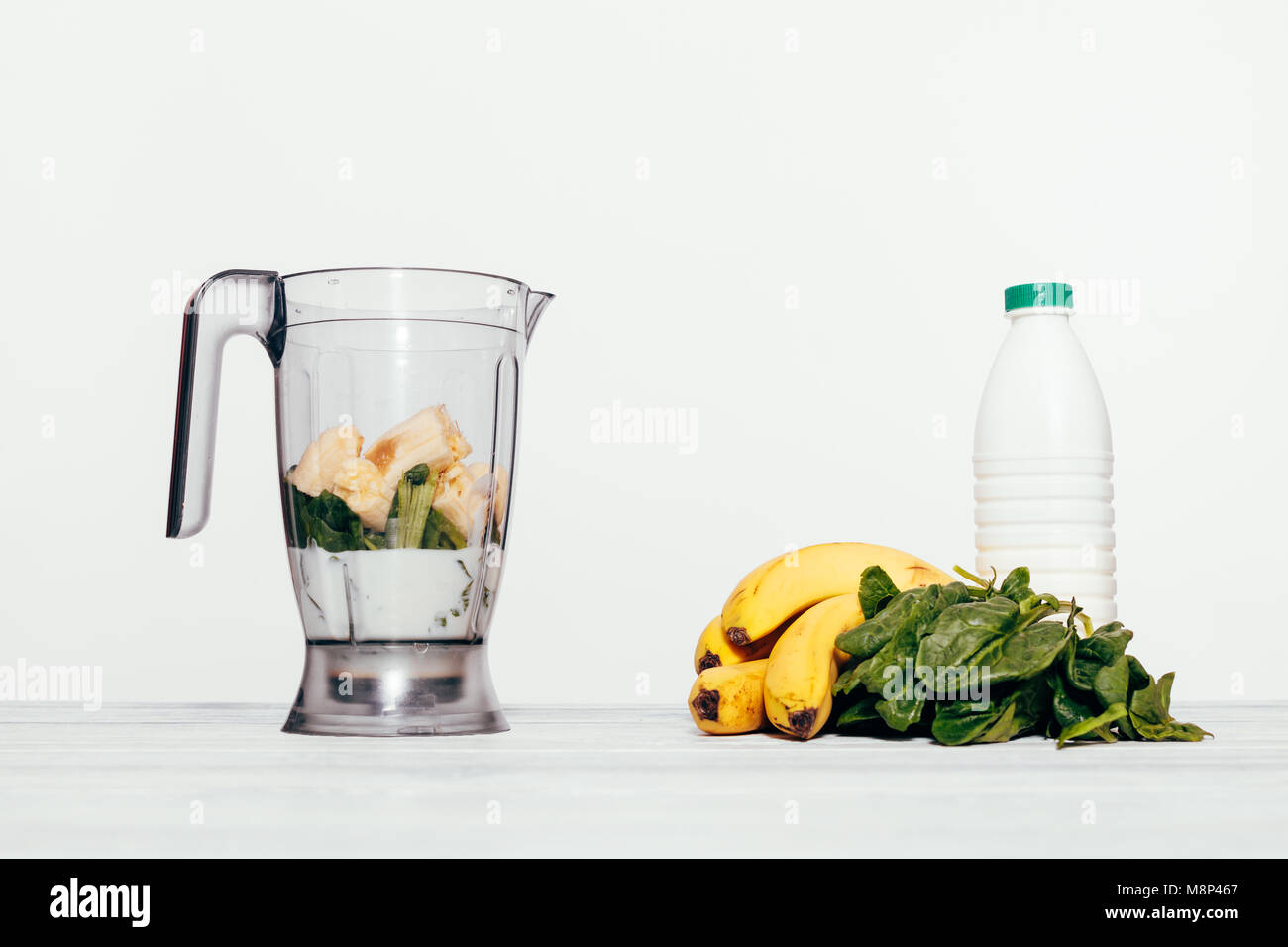 Smoothies cuisine dans un processeur de nourriture avec des bananiers, des épinards et du lait Banque D'Images