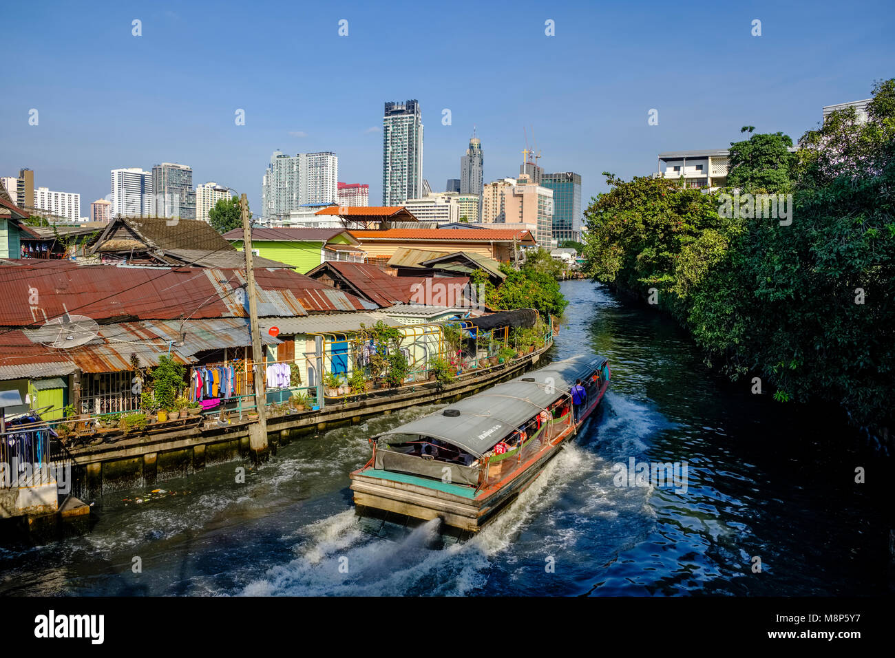 Un ferry local est conduite sur Khlong Maha Nak canal par feuille de tôle ondulée, des huttes et des immeubles de grande hauteur Banque D'Images