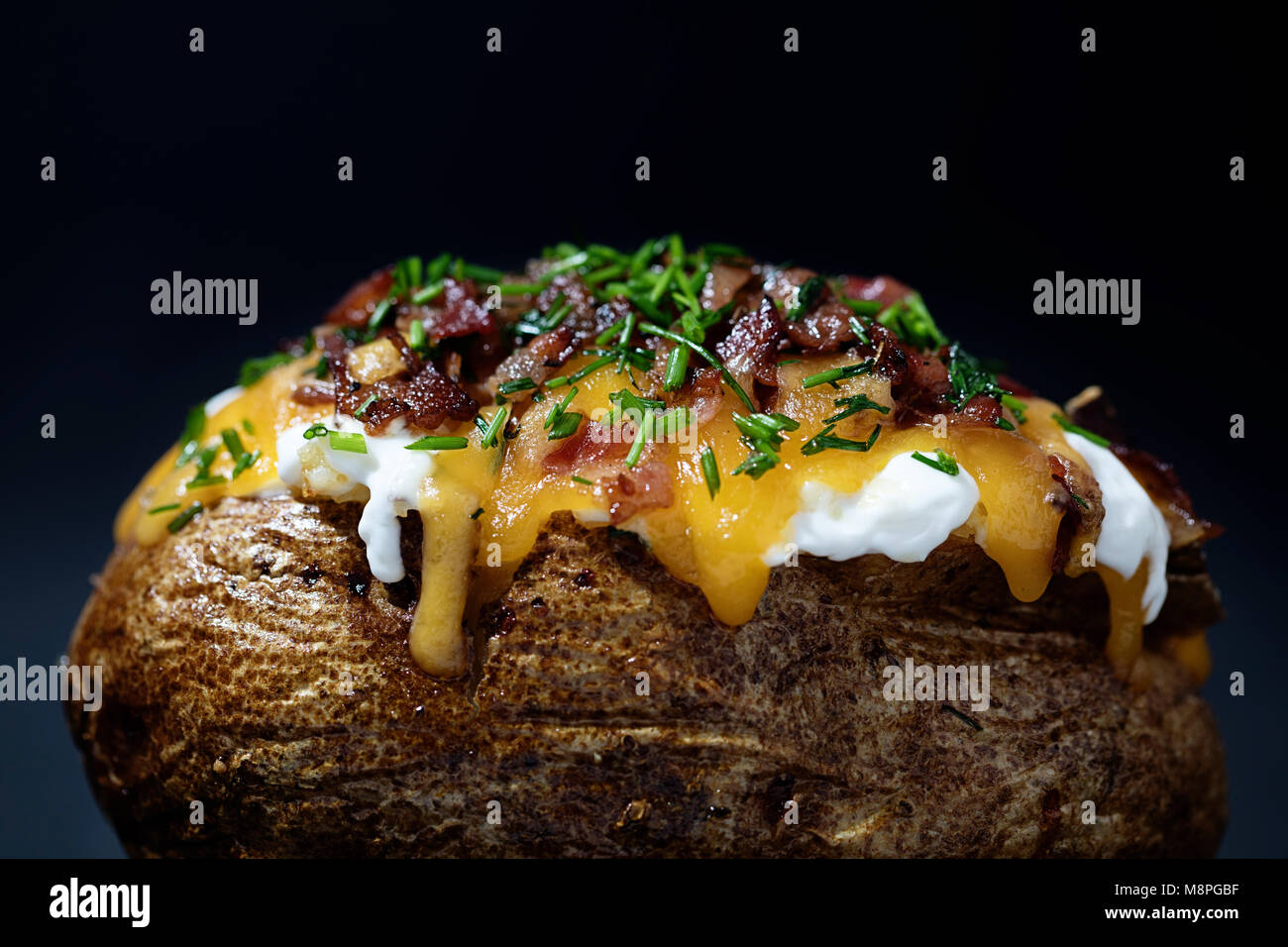 Vue latérale d'une pomme de terre au four chargé avec la ciboulette, bacon, fromage cheddar, crème sure sur noir Banque D'Images