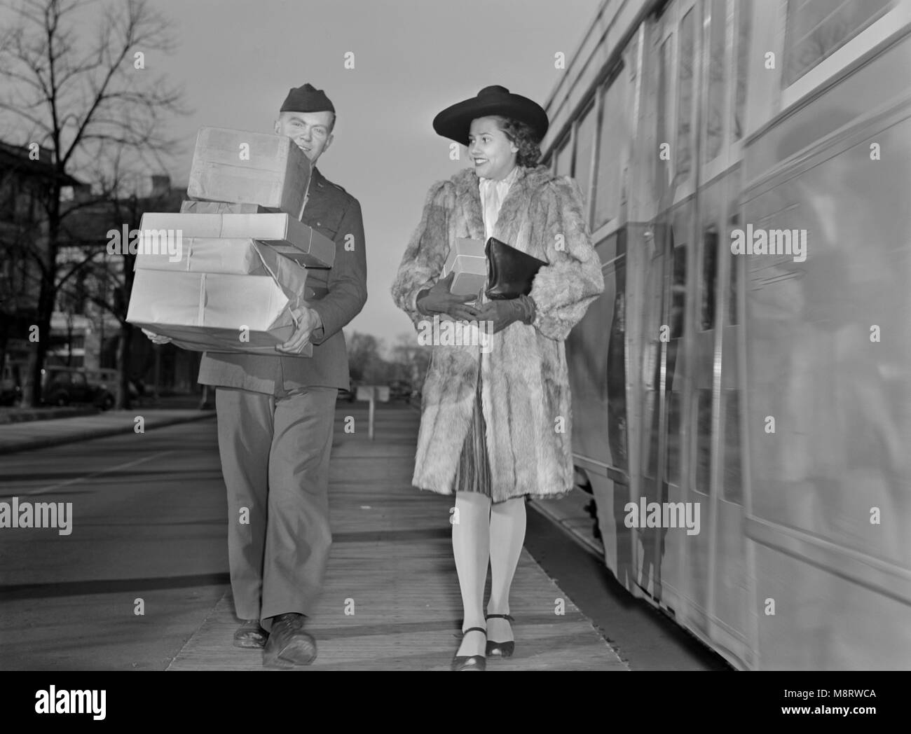 L'homme militaire transportant des colis et l'Escorte Femme à son domicile de l'arrêt de bus maintenant que la livraison des marchandises ont été réduites pour économiser sur les pneus et l'essence au cours de la Seconde Guerre mondiale, Ann Rosener pour Office of War Information, décembre 1942 Banque D'Images