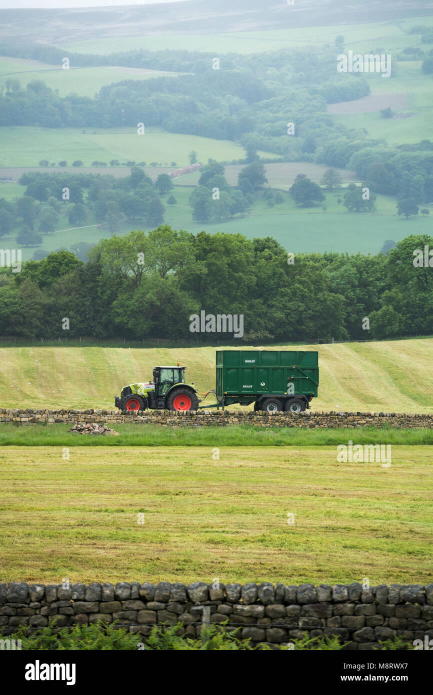 Tracteur vert avec remorque recueillaient de l'herbe pour l'ensilage, mais elles sont aujourd'hui garés en bordure du champ avec aucun pilote - West Yorkshire, Angleterre, Royaume-Uni Banque D'Images