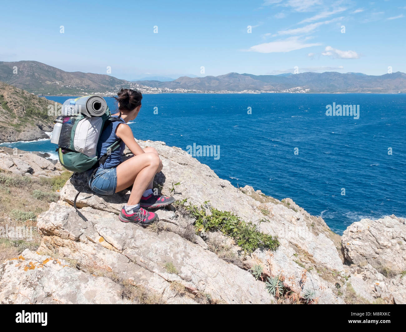 Female hiker with backpack looking at view, assis sur des rochers en mer contre montagne au cours de journée ensoleillée Banque D'Images