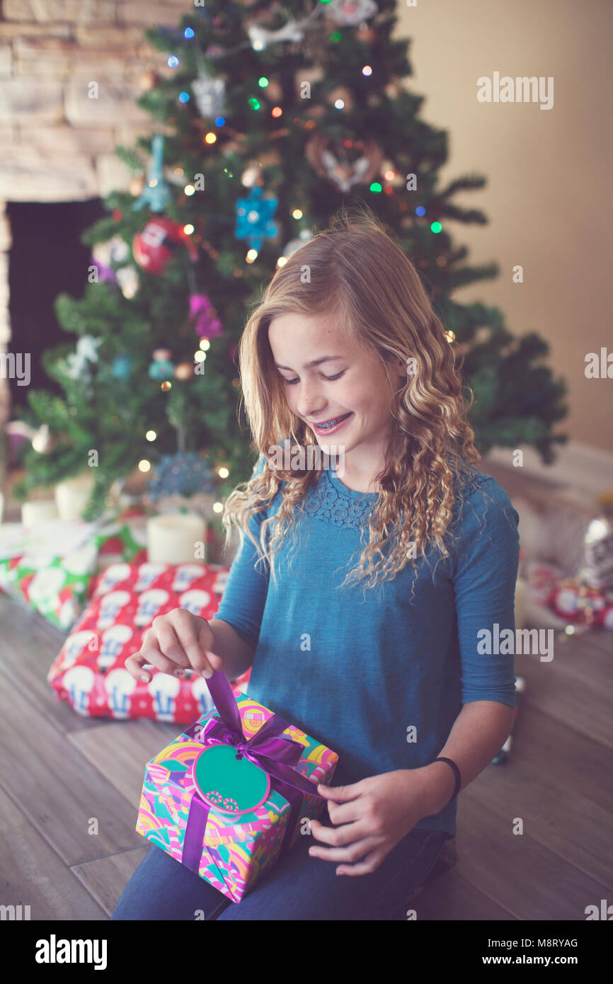 Fille tenant un cadeau de noël tout en étant assise sur le sol à la maison Banque D'Images