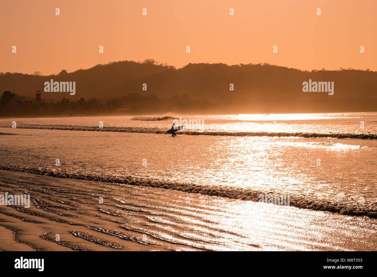 Surfer va dans ocean - silhouette de personne avec une planche de surf à la plage pendant le coucher du soleil - Banque D'Images